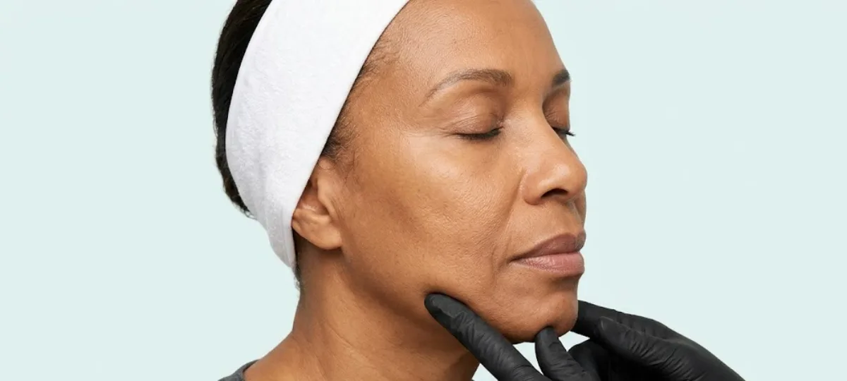 Esthetician at KiWest Spa Belleville performing a firming lifting massage along the jawline of a mature Caribbean woman during the Revival anti-aging facial in Barbados